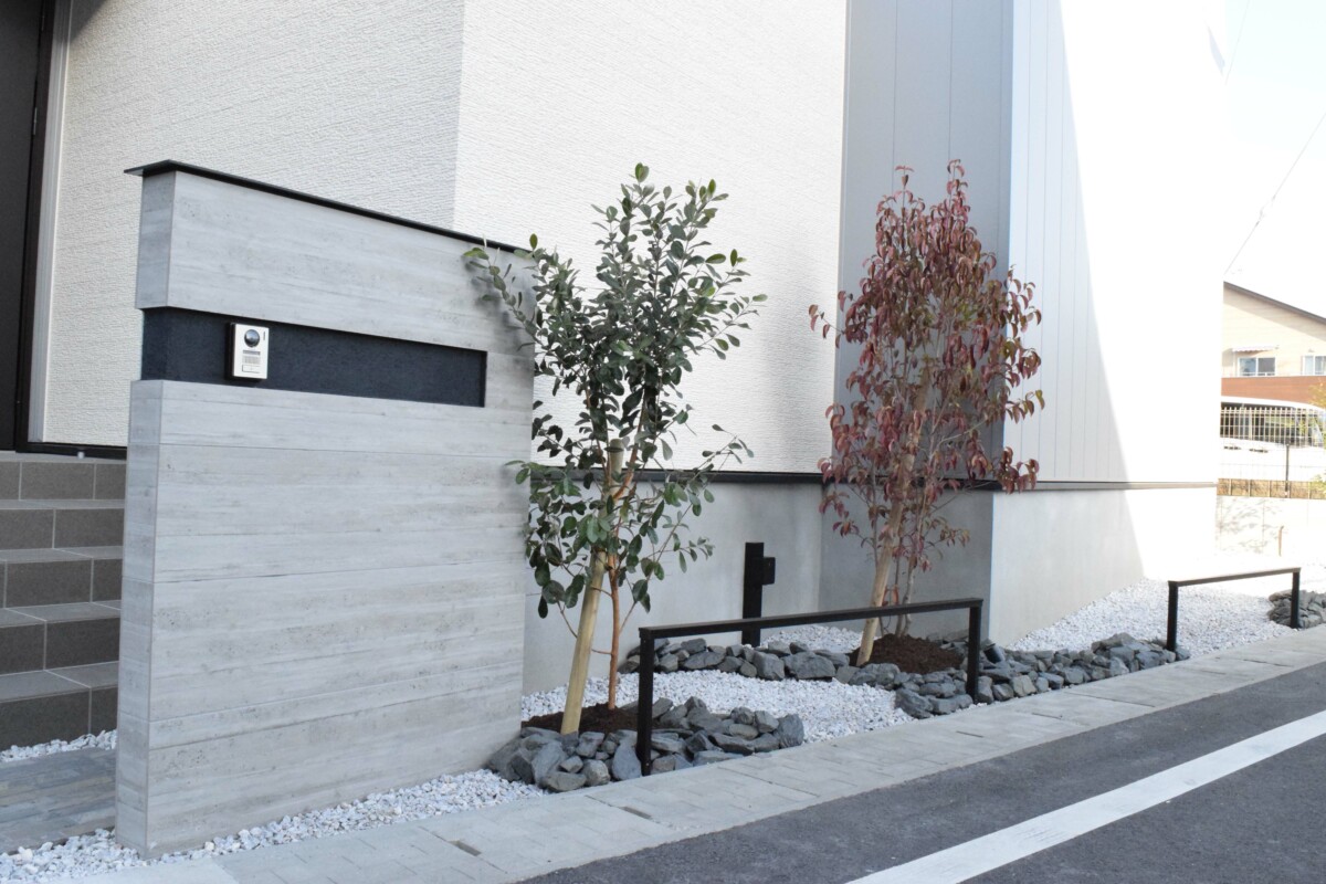 【門柱】タカショーの「セラウォール」RC杉板風タイルを使用。ブラックの意匠レールと植栽を組み合わせ、立体感のある表情に。