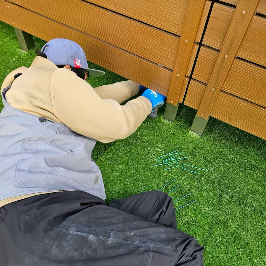 滋賀県大津市の新築外構現場にて、フェンス下の人工芝をU字ピンで丁寧に固定している施工風景。