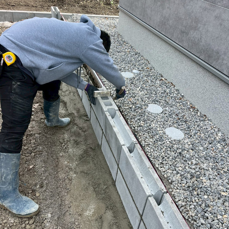 滋賀県豊郷町の新築外構現場。敷地の境界に沿って2段のコンクリートブロックを水平器で確認しながら丁寧に積んでいる様子。