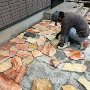 滋賀県草津市のリフォーム外構現場にて、アプローチ横に職人が乱形石を1枚ずつ並べて施工している様子。