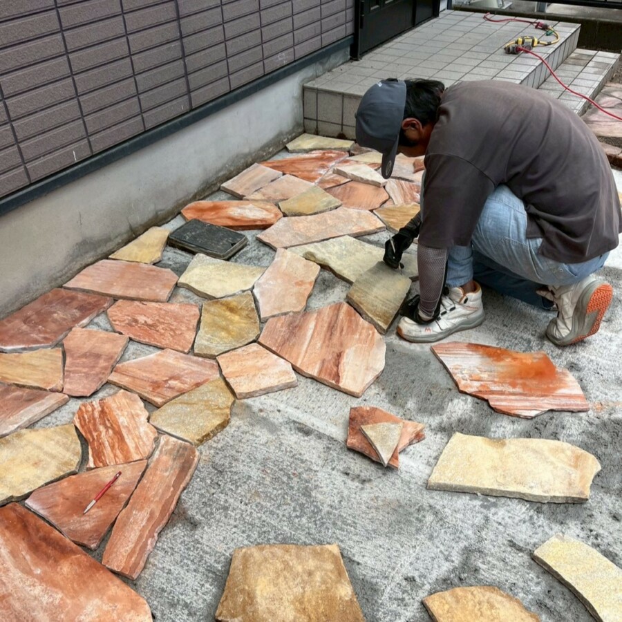 滋賀県草津市のリフォーム外構現場にて、アプローチ横に職人が乱形石を1枚ずつ並べて施工している様子。