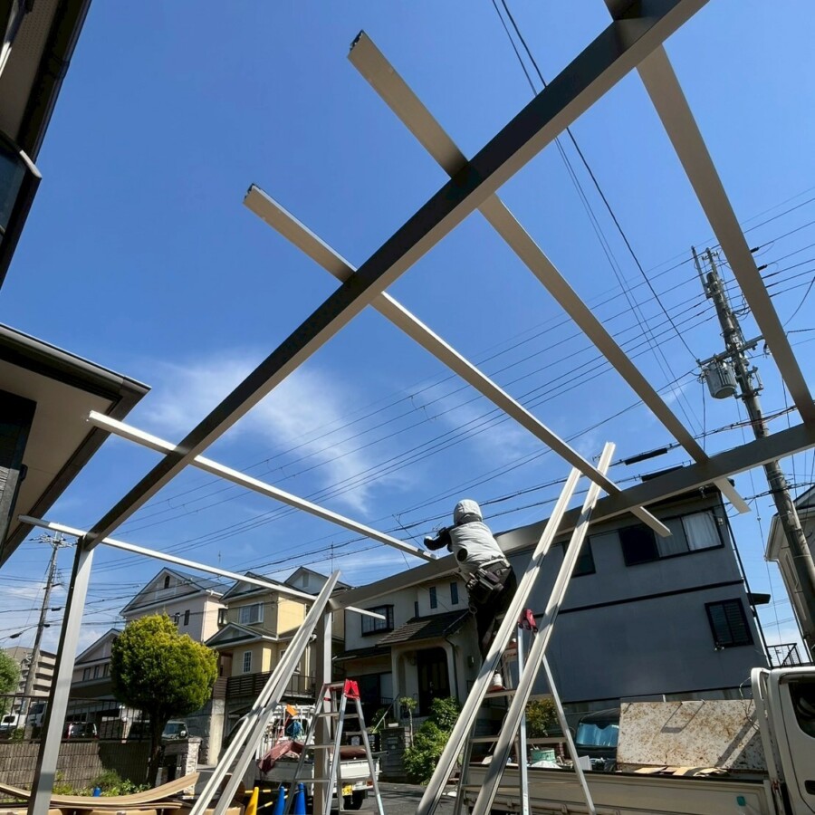 滋賀県草津市のリフォーム外構現場にて職人が高所でカーポートの梁や骨組みを組み立てている様子。