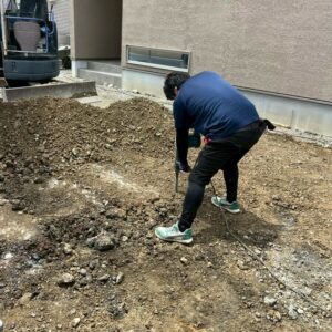 滋賀県近江八幡市の新築外構現場にて職人が工具を使い地盤の改良や調整作業を行っている様子。
