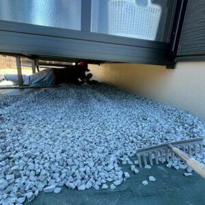 滋賀県草津市の新築外構現場にてサンルーム下の狭いスペースに職人が入り防草シートの上に砂利を敷き均している様子。