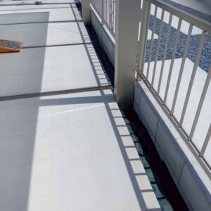 滋賀県守山市の新築外構現場にて美しく完成した土間コンクリートの横の狭い隙間に防草シートを敷いている様子。