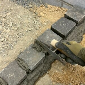 滋賀県近江八幡日の新築外構現場にて見切り部分となるピンコロ石を職人がコテを使ってモルタルで据え付けている様子。