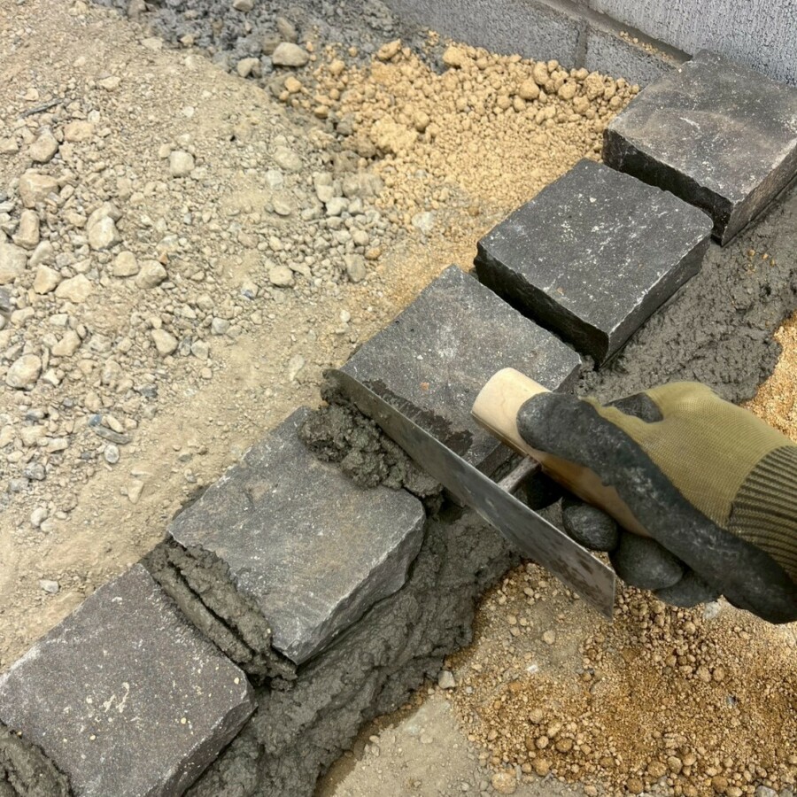 滋賀県近江八幡日の新築外構現場にて見切り部分となるピンコロ石を職人がコテを使ってモルタルで据え付けている様子。