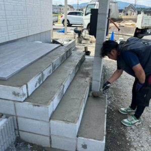 滋賀県湖南市の新築外構現場にて玄関ポーチ階段のタイル施工に向けてモルタル下地を塗る施工風景。