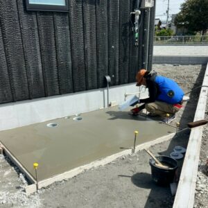 滋賀県近江八幡市の新築外構現場にて建物脇の土間コンクリート表面を金ごてで仕上げる職人の施工風景。