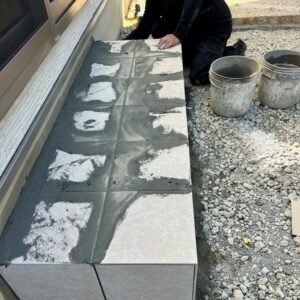 滋賀県湖南市の新築外構現場にてタイルデッキの隙間に目地材を充填する職人の施工風景。