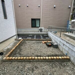 滋賀県湖南市の新築外構現場にてイエローのピンコロ石で見切りを設置した人工芝施工前とお庭奥の物置基礎スペース。