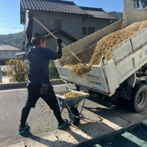 滋賀県竜王町の外構現場にて防草シートの上にダンプからサビ砂利を運搬・敷き込みする職人の施工風景。